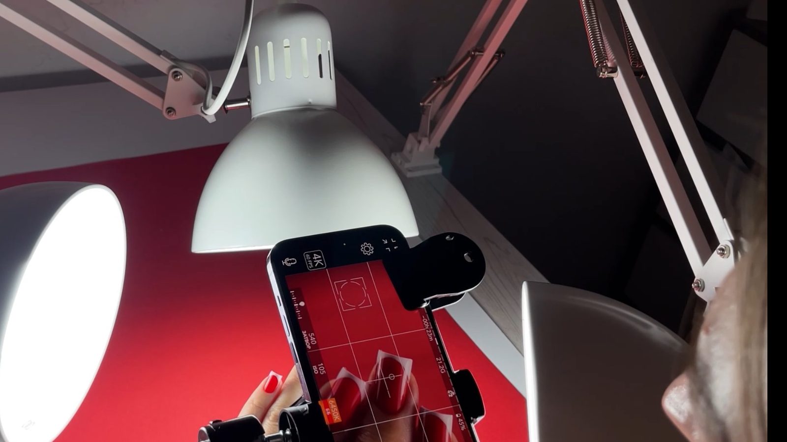 Behind the scenes: the phone camera view of red nails next to the real lighting setup
